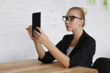 The girl sits at a table with a tablet, in a jacket and glasses. Comfortably work at home remotely via video. Copy space.