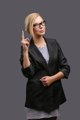 Woman, a teacher in a jacket and glasses on a gray background, expresses emotions. Copy space.