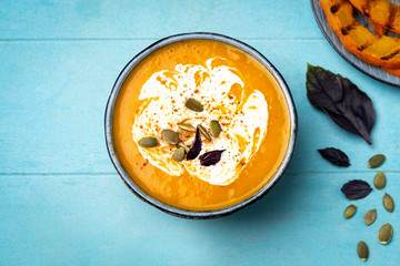 Pumpkin soup in a plate on a blue wooden background, top view. Slices of grilled pumpkin. Copy space.