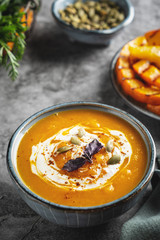 Pumpkin cream soup in the bowl, close-up.  Slices of grilled pumpkin. Gray background.