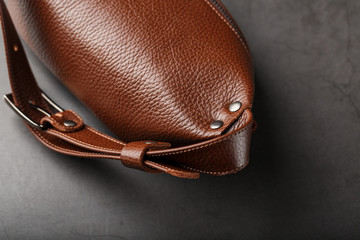 A brown belt bag made of textured brown leather on a black stone background. Elegant fanny pack brown bag with a zipper