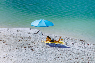 woman in swimsuit walking by sand beach blue sun umbrella and yellow blanket