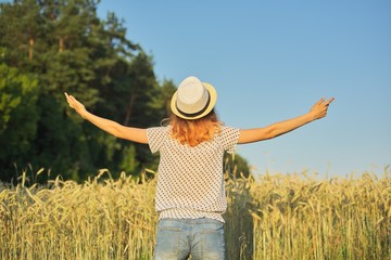 Girl in hat in wheat field with her backs with open hands