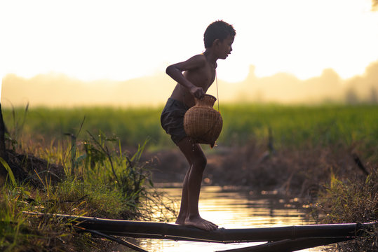 Asian little child fisherman holding fish trap walking along the river in the morning.