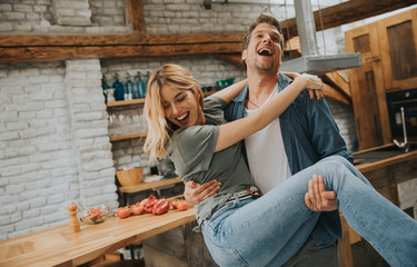 Happy couple enjoy each other in the modern kitchen while man holding woman on hands