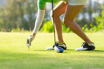 Hand asian sporty woman putting golf ball on tee with club in golf course on evening on time for healthy sport. Lifestyle and Sport Concept