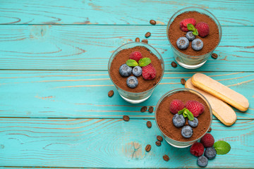 Classic tiramisu dessert with blueberries and strawberries in a glass cup and savoiardi cookies on wooden background