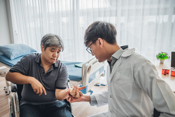 Asian male doctor is checking the hand with a kink of middle aged male patients Which is a...