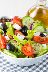 Fresh Greek salad made of cherry tomato, ruccola, arugula, feta, olives, cucumbers, onion and spices. Caesar salad in a white bowl on wooden background. Healthy organic diet food concept.