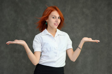 Photo Portrait of a cute girl woman with bright red hair manager in a white shirt on a gray background in the studio. He talks, shows his hands in front of the camera with emotions.