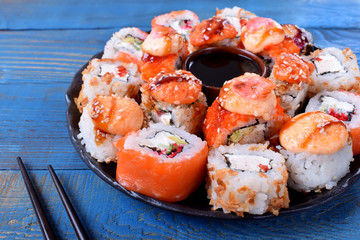 Sushi rolls assortment and soy sauce served on round plate on blue wooden table
