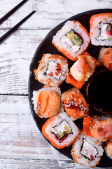 Sushi rolls assortment and soy sauce served on round plate on white wooden table