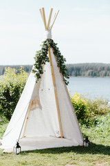 Wooden fabric wigwam decorated with green eucalyptus branches in backyard, event or wedding in boho...