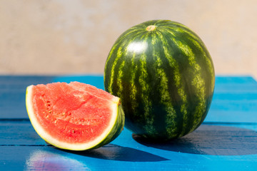 Melancia Baby inteira, cortada em pedaços sobre a mesa de madeira na cor azul frança