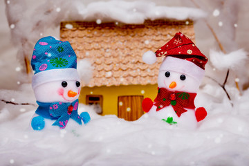 Two toy snowmen near the house during snowfall_