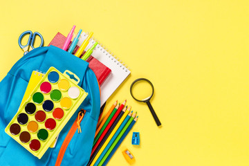 School backpack with stationery on yellow background.