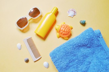 Trendy sunglasses, wooden comb, yellow sunscreen bottle, rubber toy turtle, blue towel and seashells. Flat lay summer holiday photo. Top view beach essentials