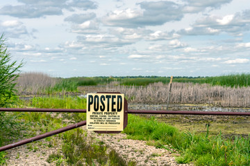 Yellow and black Private Property sign hangs on a fence in front of an open field. Concepts of outdoors, public and private lands