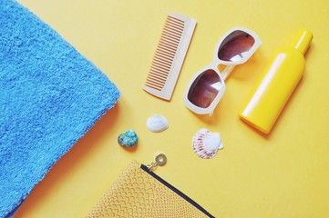 Flat lay beach photo, accessories for vacation. Blue towel, cosmetic bag, sunglasses, sunscreen bottle on a yellow background