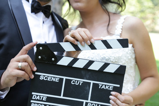 Happy beautiful bride and groom, woman holds clapper board, cinema board 