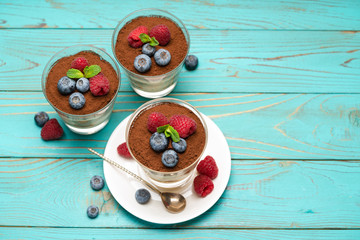 Classic tiramisu dessert with blueberries and strawberries in a glass cup on wooden background