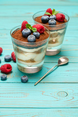 Classic tiramisu dessert with blueberries and strawberries in a glass cup on wooden background