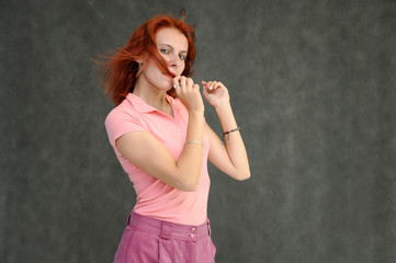 Obraz premium Photo Portrait of a cute woman girl with bright red hair in a peach t-shirt and pink skirt on a gray background in the studio. He talks, shows his hands in front of the camera with emotions.