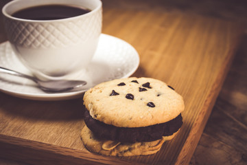 Obraz na płótnie Canvas Cookie butter and chocolate Cookies stacked 3 pieces, black coffee in the cup white on white coasters,and stainless steel spoon are on a wooden tray , all placed on a wooden table.