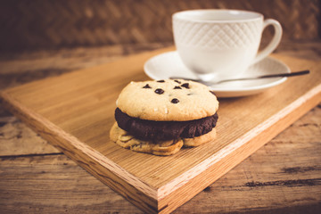 Cookie butter and chocolate Cookies stacked 3 pieces, black coffee in the cup white on white coasters,and stainless steel spoon are on a wooden tray ,  all placed on a wooden table.