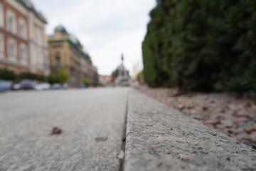 Paving slabs close-up on the background of streets, old buildings are in blur. Sharpness on granite tile. Square and houses are blurred in the background. The street is removed from the lower angle.