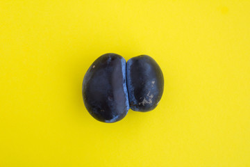 Ugly food. Ugly blue plum  in the center of the yellow  background. Top view. Copy space.