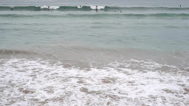 Evening ocean surf. Foamy waves fill the sandy beach. Surfers straddled the wave. A large group is waiting