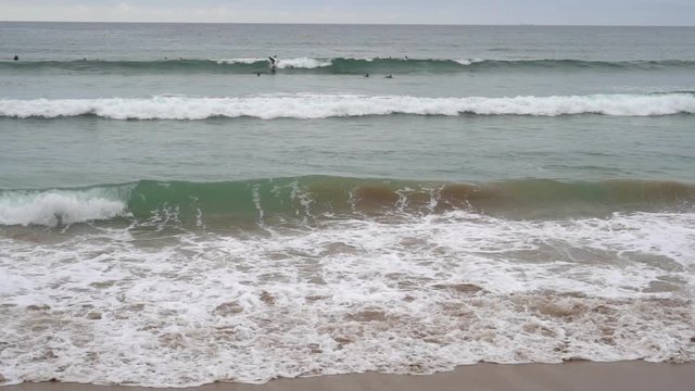 Evening ocean surf. Foamy waves fill the sandy beach. Surfers straddled the wave. A large group is waiting