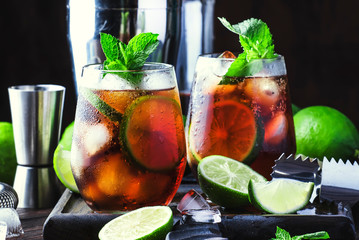Cuba libre alcohol cocktail with golden rum, lemon juice, cola, lime and ice, dark bar counter...