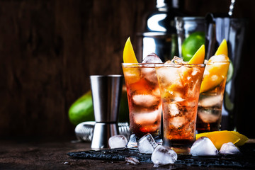 Alcoholic cocktail with mango, cranberries, lime, crushed ice and liquor, dark wooden bar counter background, selective focus