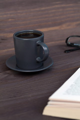 dark cup of coffee with book on wooden table