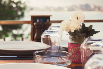 Served table in a summer cafe. The sea in the background. Wooden furniture, white flowers.