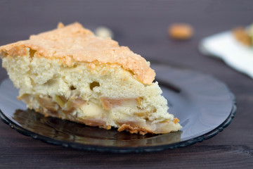 piece of apple pie. Cake with apples on dark glass plate on a wooden background