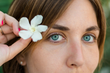 Close up portrait of a young woman with blue eyes with green plants on the background