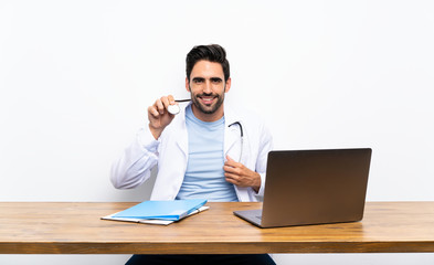 Young doctor man with his laptop over isolated wall