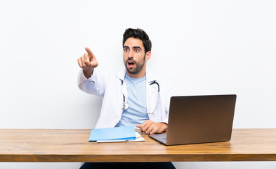 Young doctor man with his laptop over isolated wall pointing away