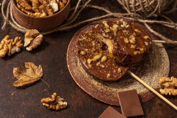 Slices of apples in chocolate, caramel glaze and walnuts on skewers on a dark background