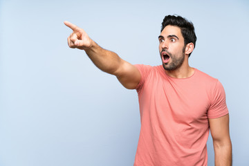 Handsome young man in pink shirt over isolated blue background pointing away