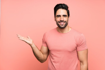 Handsome young man over isolated pink background holding copyspace imaginary on the palm