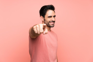 Handsome young man over isolated pink background points finger at you