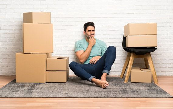Handsome young man moving in new home among boxes thinking an idea