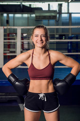 Strong woman in a black gloves standing in front of boxing ring