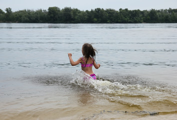 Girl in swim suit is running into the river to swim; summer entertainment