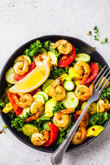 Shrimp, avocado and vegetable salad in a black dish on gray background, top view.
