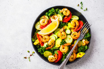 Shrimp, avocado and vegetable salad in a black dish on gray background, top view.